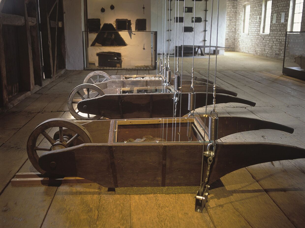 3 Schubkarren aus Holz, jeweils bis obenhin gefüllt mit Erz, Holzkohle und Kalkstein. 